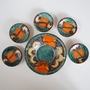 Könnte beinhalten: Satz von sechs Keramiktellern mit einem geometrischen Design in Blau, Grün, Orange und Weiß. Die Teller sind in verschiedenen Größen und mit verschiedenen Mustern.