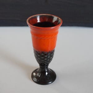 Op de afbeelding: Een zwarte en oranje keramische beker met een getextureerde basis. De beker heeft een brede rand en een smalle basis.