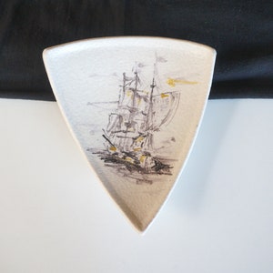 May include: A white ceramic triangular dish with a black and gold illustration of a sailing ship.