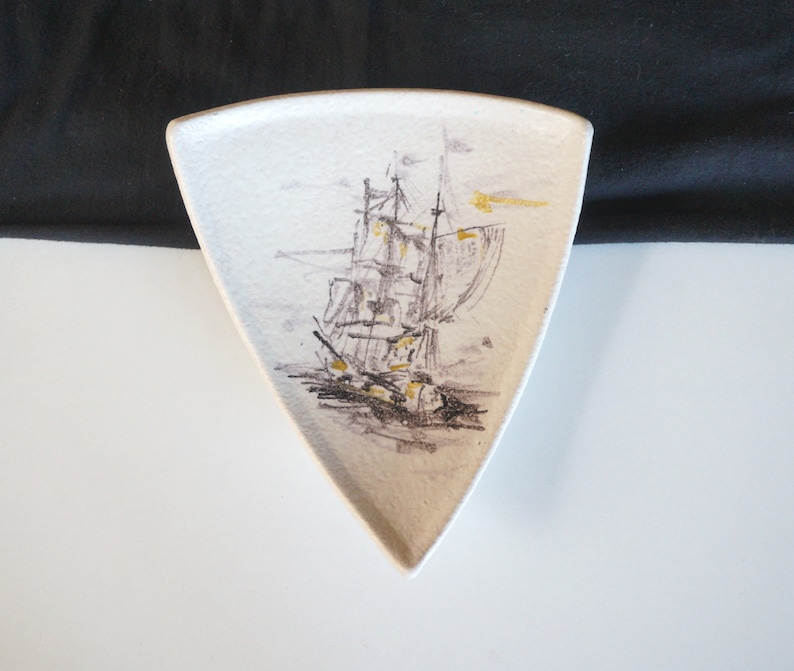 May include: A white ceramic triangular dish with a black and gold illustration of a sailing ship.