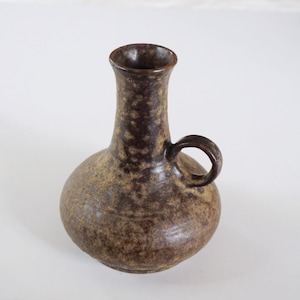Könnte beinhalten: Eine braune und beigefarbene Keramikvase mit einem gesprenkelten Überzug und einem einzigen Henkel. Die Vase hat einen schmalen Hals und einen runden Körper.