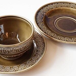 May include: A set of two green ceramic teacups and saucers with a decorative pattern around the rim.