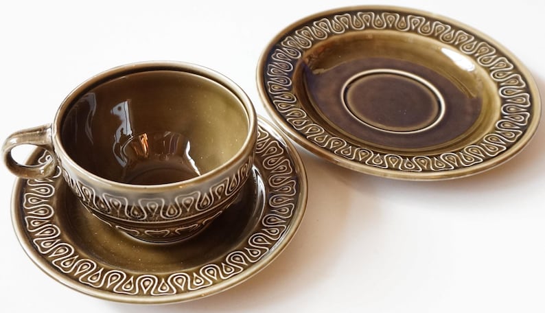 May include: A set of two green ceramic teacups and saucers with a decorative pattern around the rim.