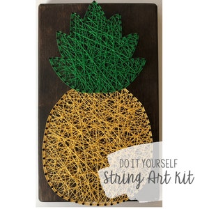 Op de afbeelding: DIY string art-set met een ananasontwerp met groene bladeren en een geel lichaam. De set bevat alle materialen die nodig zijn om het kunstwerk te maken.