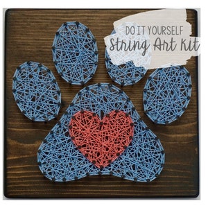 May include: DIY string art kit featuring a paw print with a heart in the centre. The paw print is made with blue string and the heart is made with red string. The background is a dark brown wooden board. The text "DO IT YOURSELF String Art Kit" is written in white on a white background.
