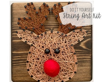 May include: DIY string art kit featuring a reindeer design with a red nose. The reindeer is made with brown string wrapped around black nails on a wooden board.