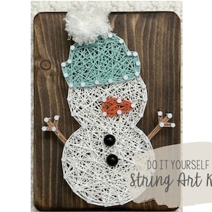 May include: String art kit featuring a snowman design. The snowman is crafted with white string on a dark wooden board, wearing a teal hat and an orange nose. The text "DO IT YOURSELF String Art Kit" is visible.