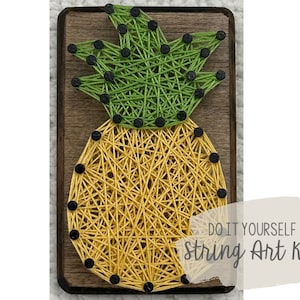 Op de afbeelding: Een DIY string art kit met een ananasontwerp. De ananas is gemaakt van gele en groene draad gewikkeld rond zwarte spijkers op een houten plank. De tekst "DO IT YOURSELF String Art Kit" is zichtbaar onderaan de afbeelding.
