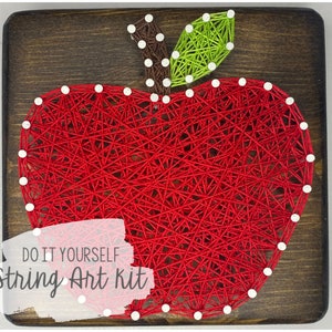 May include: DIY string art kit featuring a red apple with a green leaf. The kit includes all the materials needed to create the artwork, including string, nails, and a wooden base.