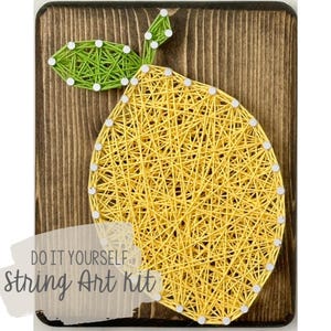 May include: DIY string art kit featuring a yellow lemon with green leaves on a wooden background. The text "Do It Yourself String Art Kit" is printed below the lemon.