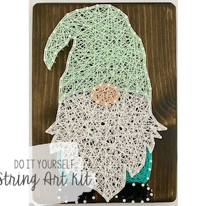 May include: DIY string art kit featuring a gnome with a green hat, white beard, and turquoise accents. The kit includes a wooden base, string, and nails.