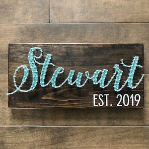Può includere: Un cartello di legno con il nome "Stewart" scritto in arte di filo blu. Il cartello include anche il testo "EST. 2019" in bianco.