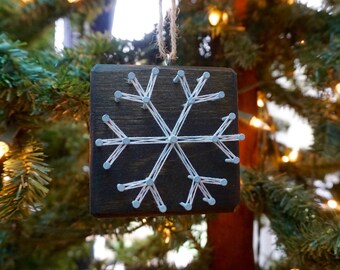 Peut inclure: Une décoration de flocon de neige en ficelle blanche sur un fond de bois brun foncé. Le flocon de neige est fait avec de la ficelle blanche enroulée autour de clous enfoncés dans le bois.