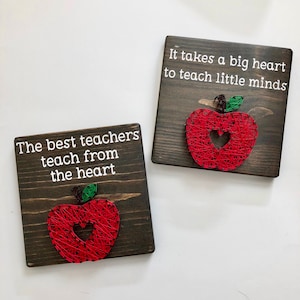 Op de afbeelding: Twee houten borden met rode appel string art en witte tekst. Het eerste bord zegt "De beste leraren leren vanuit het hart". Het tweede bord zegt "Het kost een groot hart om kleine geesten te leren".