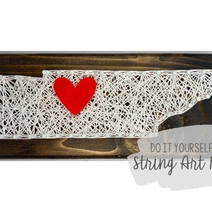 Peut inclure: Kit de broderie en fil pour créer une œuvre d'art représentant la silhouette de l'état du Tennessee avec un cœur rouge au centre. Le kit comprend tous les matériaux nécessaires à la création de l'œuvre, y compris le fil, les clous et une base en bois.  "Do It Yourself String Art Kit" est écrit sous l'œuvre.