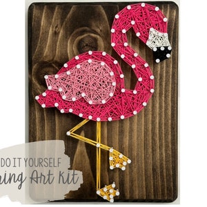 May include: Pink flamingo string art kit on a wooden background. The kit includes all the materials needed to create the art, including string, nails, and a wooden board.