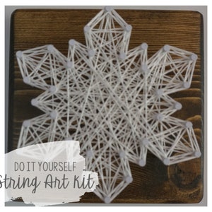 May include: White string art snowflake kit on a dark wood background.  The kit includes all the materials needed to create the snowflake, including string, nails, and a wooden base.  DO IT YOURSELF string Art Kit.