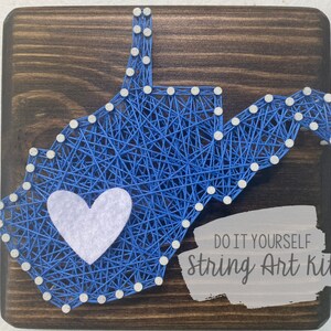 Peut inclure: Un kit de broderie en fil DIY représentant l'état de Virginie-Occidentale avec un cœur blanc au centre. Le kit est sur une base en bois et comprend le texte "DO IT YOURSELF String Art Kit".