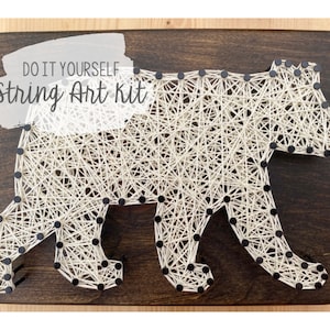 May include: DIY string art kit featuring a bear design. The bear is made of white string wrapped around black nails on a wooden board.