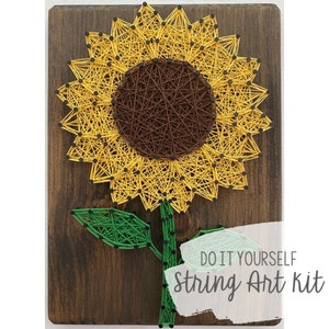 Pode incluir: Kit de arte de fio DIY com um girassol com um centro marrom e pétalas amarelas. O girassol está em um fundo de madeira com o texto "DO IT YOURSELF string Art kit".