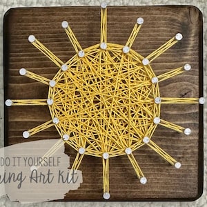 Op de afbeelding: DIY string art kit met een geel zonontwerp op een houten achtergrond. De tekst "DO IT YOURSELF string Art kit" is onder de zon gedrukt.