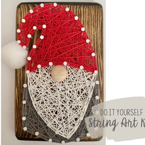May include: DIY string art kit featuring a Santa Claus design with a red hat, white beard, and gray beard trim. The kit is on a wooden base.
