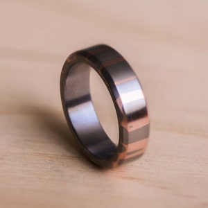 May include: A silver ring with a rose gold inlay design. The ring is made of metal and has a polished finish.