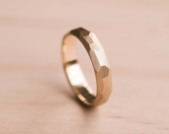 May include: A gold ring with a textured, faceted design. The ring is made of hammered metal and has a polished finish.