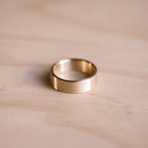 May include: A gold-colored ring with a brushed finish. The ring is simple and elegant.