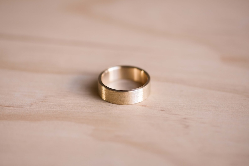 May include: A gold-colored ring with a brushed finish. The ring is simple and elegant.