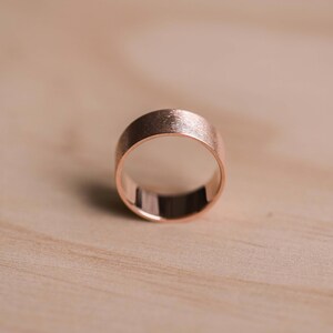 May include: A simple rose gold band ring with a brushed finish.
