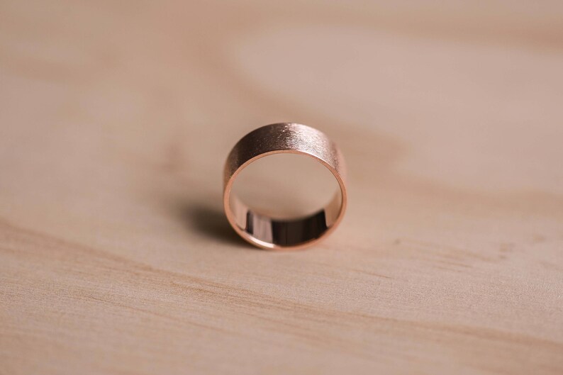 May include: A simple rose gold band ring with a brushed finish.