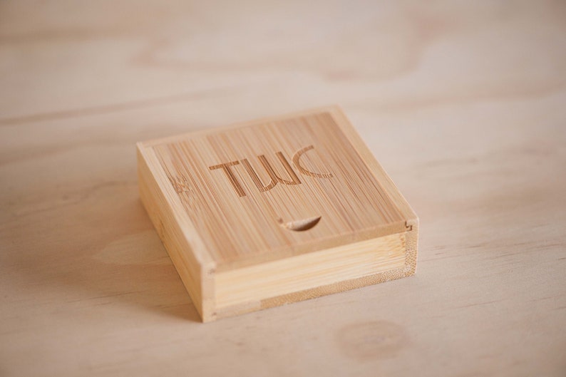 May include: A small, square, wooden box with the word "TWIC" engraved on the top. The box is made of light brown bamboo.