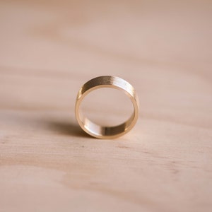 May include: A simple gold band ring with a brushed finish.