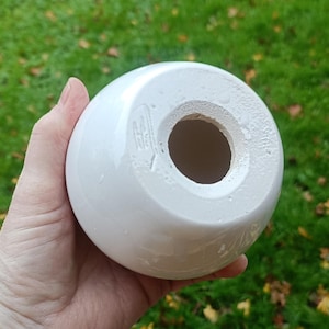 May include: A white, spherical ceramic object with a large central opening. The object has a glossy finish and appears to be a decorative item or a part of a larger piece. The base has a rough, unglazed texture.