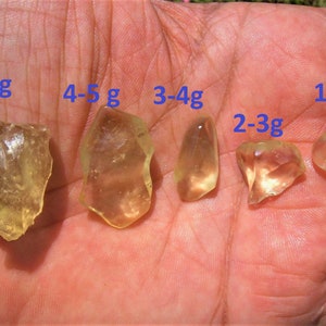 Może przedstawiać: Pięć kawałków przezroczystych kryształów kwarcu o żółtawym odcieniu, o różnych rozmiarach, od 1-2 gramów do 5-6 gramów. Kryształy są prezentowane na dłoni, z oznaczeniem ich wagi w gramach.