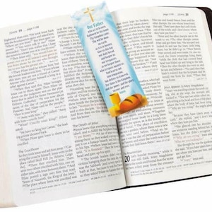 May include: An open Bible with a bookmark featuring a blue sky, a chalice, and bread. The bookmark text reads "Our Father, who art in heaven, hallowed be thy name. Thy kingdom come, thy will be done, on earth as it is in heaven. Give us this day our daily bread, and forgive us our trespasses, as we forgive those who trespass against us. And lead us not into temptation, but deliver us from evil. For thine is the kingdom, and the power, and the glory, forever and ever. Amen."