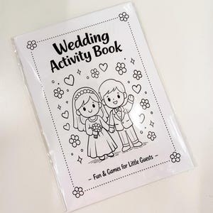 May include: A white paper wedding activity book in a clear plastic sleeve. The cover features black line art of a bride and groom surrounded by hearts, flowers, and stars. The text reads Wedding Activity Book and Fun & Games for Little Guests.