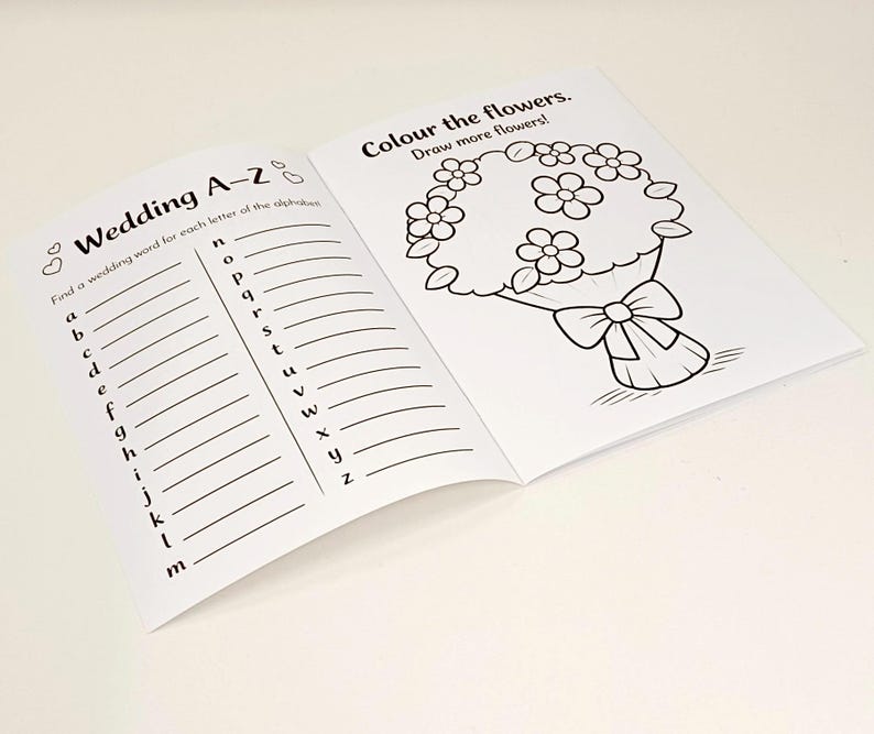 May include: An open activity book with black and white printed pages. The left page features a Wedding A-Z list with lines for writing. The right page shows a line art illustration of a flower bouquet with the text Colour the flowers. Draw more flowers!