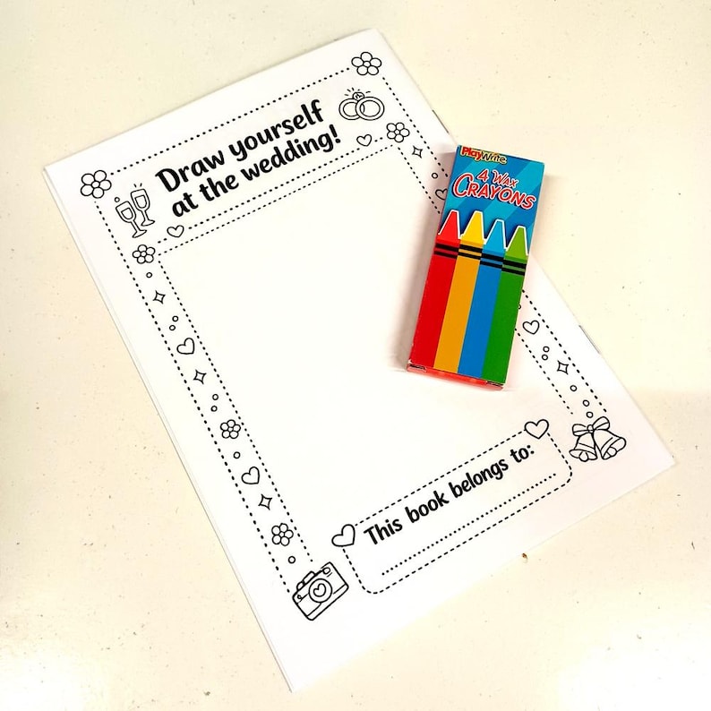 May include: A white paper activity sheet with a black outline border featuring wedding-themed icons like rings, flowers, and bells. The text reads Draw yourself at the wedding and This book belongs to. A small box of four wax crayons is placed on top.