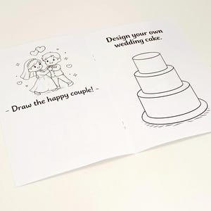 May include: An open activity book with white pages featuring black line art. The left page shows a cartoon couple with the text Draw the happy couple! The right page displays a three-tiered wedding cake with the text Design your own wedding cake.