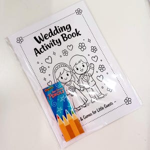 May include: A white wedding activity book with black line art of a bride and groom, hearts, and flowers, featuring the text Wedding Activity Book and Games for Little Guests. A small box of PlayWrite mini color pencils is placed on the front.