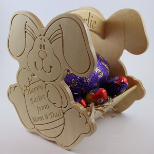 May include: Wooden Easter bunny basket with a personalised name tag that says "Charlie". The basket is filled with chocolate eggs and has a message that says "Happy Easter from Mom & Dad".