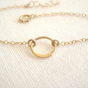 May include: A delicate gold-colored chain bracelet with a circular pendant. The bracelet features a small, open circle as a focal point, connected to a fine chain with a lobster clasp. The jewelry is displayed on a white surface.