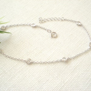 May include: A silver anklet with a delicate chain and small round clear stones.