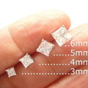 May include: A selection of square-cut, clear cubic zirconia stud earrings in various sizes, ranging from 3mm to 6mm. The earrings are set in a silver-colored metal, showcasing their sparkling facets. The image includes size indicators.