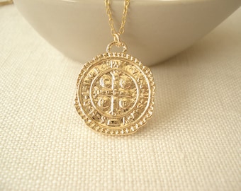 May include: A gold chain necklace with a large, round pendant featuring a detailed, embossed design. The pendant has a cross with four circles and Latin text around the edge.