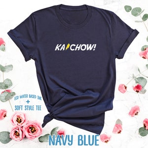 Op de afbeelding: Donkerblauw t-shirt met een gele bliksem en de tekst "KACHOW!" gedrukt op de voorkant. Het shirt is gemaakt van een zacht, comfortabel materiaal.