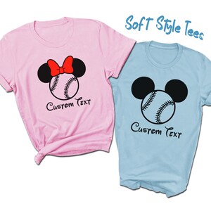 May include: Two soft style t-shirts, one pink and one light blue, with a baseball and Mickey Mouse ears design. The pink shirt has a red bow on the Mickey Mouse ears. Both shirts say "Custom Text" underneath the design.