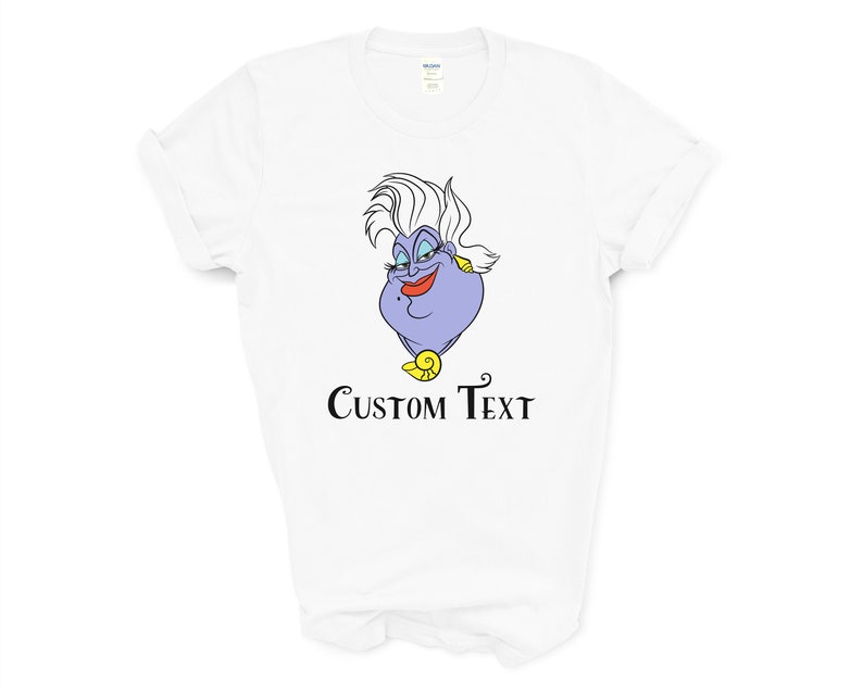以下が含まれることがあります： 白いTシャツに、リトルマーメイドのウルスラの漫画の画像がプリントされています。画像の下には「CUSTOM TEXT」という文字がプリントされています。